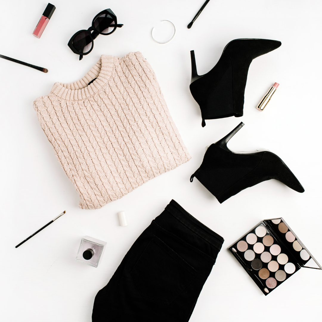 Women fashion flat lay with beige sweater, black jeans, black ankle booties with makeup and sunglasses on a white background