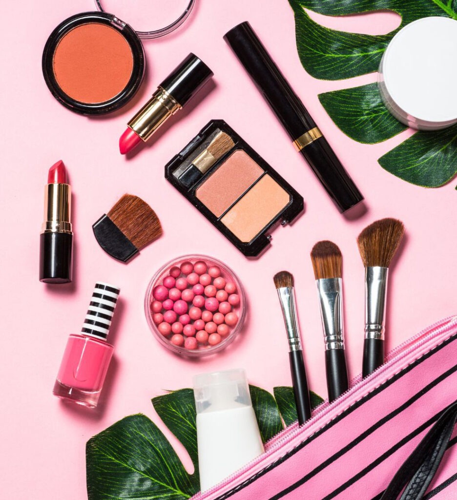 Top view of cosmetics out of makeup bag on a pink background
