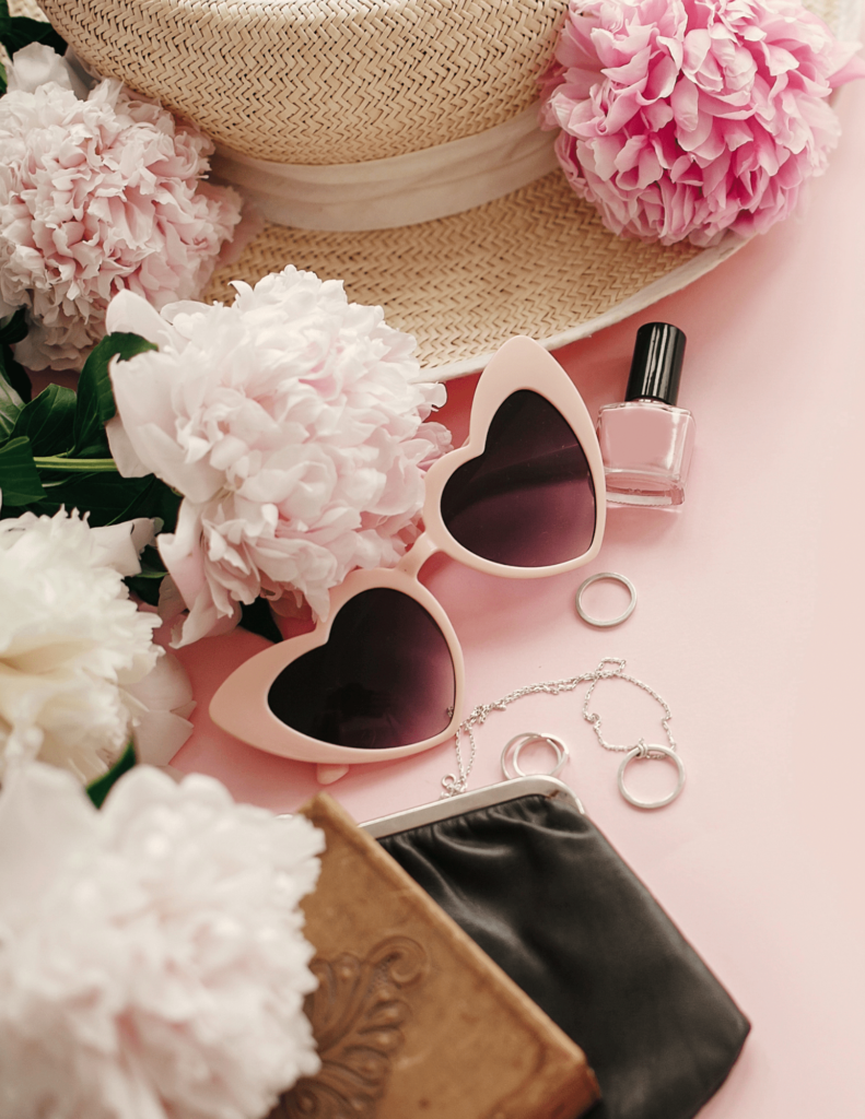Pink girly flat lay of retro pink sunglasses, pink peonies, jewelry and straw hat