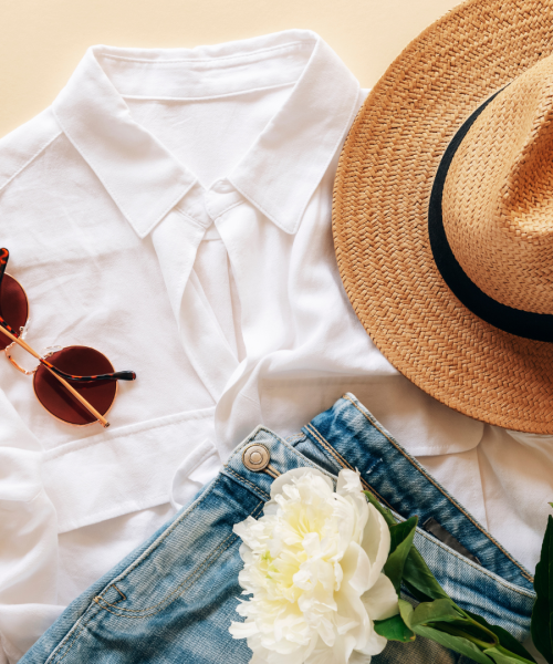 Feminine summer fashion flat lay with white top, jeans, sunglasses, straw hat and white peony flower on beige background